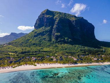 Le Morne plajı Mauritius, Tropikal plaj palmiye ağaçları ve beyaz kum mavisi okyanus ve şemsiyeli plaj yatakları, güneş sandalyeleri ve güneş şemsiyeleri bir palmiye ağacının altında, Le Morne plajı Mauritius 'ta.