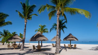 Le Morne beach Mauritius,Tropical beach with palm trees and white sand blue ocean and beach beds with umbrella,Sun chairs and parasol under a palm tree at a tropical beac, Le Morne beach Mauritius