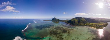 Le Morne plajı Mauritius, Tropikal plaj palmiye ağaçları ve beyaz kum mavisi okyanus ve şemsiyeli plaj yatakları, güneş sandalyeleri ve güneş şemsiyeleri bir palmiye ağacının altında, Le Morne plajı Mauritius 'ta.
