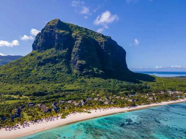 Le Morne plajı Mauritius, Tropikal plaj palmiye ağaçları ve beyaz kum mavisi okyanus ve şemsiyeli plaj yatakları, güneş sandalyeleri ve güneş şemsiyeleri bir palmiye ağacının altında, Le Morne plajı Mauritius 'ta.