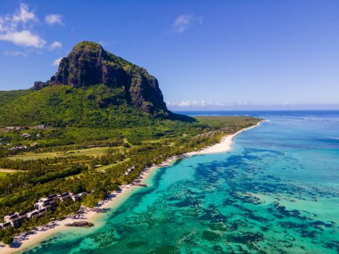 Le Morne plajı Mauritius, Tropikal plaj palmiye ağaçları ve beyaz kum mavisi okyanus ve şemsiyeli plaj yatakları, güneş sandalyeleri ve güneş şemsiyeleri bir palmiye ağacının altında, Le Morne plajı Mauritius 'ta.