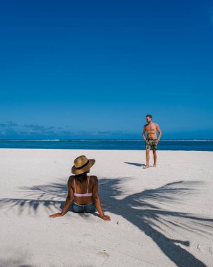 Le Morne plajı Mauritius, Tropikal plaj palmiye ağaçları ve beyaz kum mavisi okyanus. Tatil sırasında sahilde yürüyen çift ve kadın.