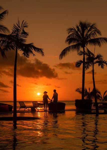 Pár férfi és nő nézi naplementét Mauritius trópusi strandján pálmafákkal a medence mellett, Trópusi naplemente Mauritius strandján — Stock Fotó