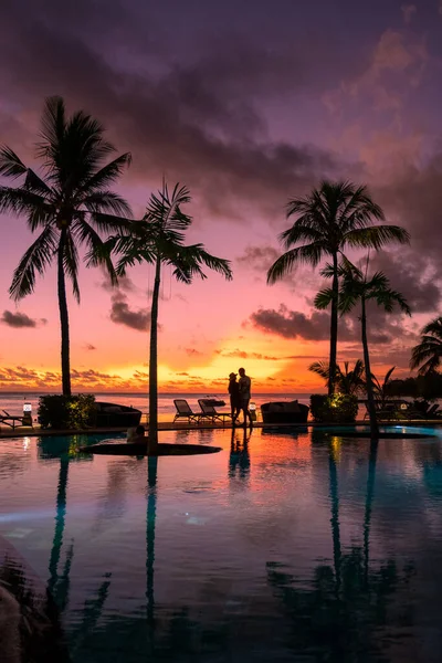 Couple men and woman watching sunset on a tropical beach in Mauritius with palm trees by the swimming pool, Tropical sunset on the beach in Mauritius — Fotografia de Stock