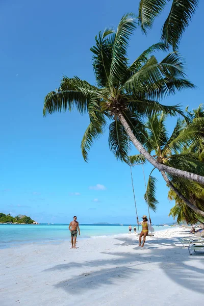 Praslin Seychelles tropical island with withe beaches and palm trees, couple men and woman in hammock swing on the beach under a palm tree at Anse Volber Seychelles — Stockfoto