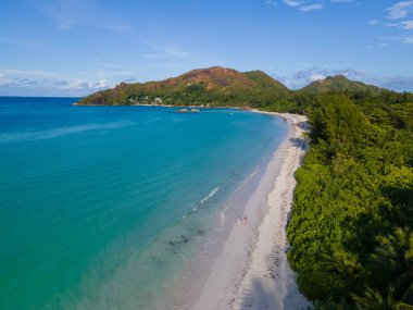 Praslin Seyşeller 'in kumsalının insansız hava görüntüsü Anse Volbert, kumsalda yürüyen birkaç kadın ve erkek.