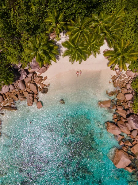 ビーチやヤシの木があるプラスリンセイシェル熱帯の島、 Anseラツィオの熱帯ビーチを訪れるセーシェルでの休暇中のカップルの男性と女性プラスリンセイシェルのドローンビュー — ストック写真