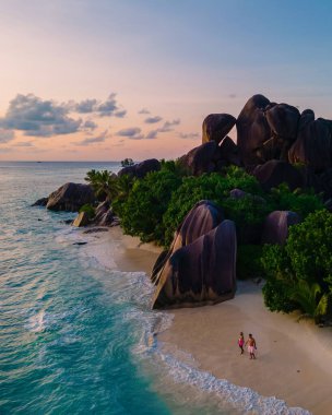 Anse Source dArgent plajı, La Digue Adası, Seyshelles, İHA hava görüntüsü La Digue Seyşelles kuş bakışı, gün batımında sahilde yürüyen birkaç erkek ve kadın lüks bir tatilde