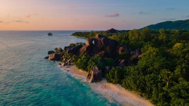 Anse Source dArgent plajı, La Digue Adası, Seyshelles, İHA hava görüntüsü La Digue Seyşelles kuş bakışı, gün batımında sahilde yürüyen birkaç erkek ve kadın lüks bir tatilde
