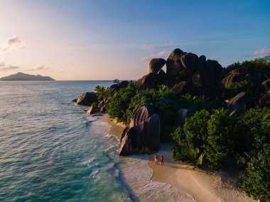 Anse Source dArgent plajı, La Digue Adası, Seyshelles, İHA hava görüntüsü La Digue Seyşelles kuş bakışı, gün batımında sahilde yürüyen birkaç erkek ve kadın lüks bir tatilde