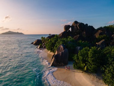 Anse Source dArgent plajı, La Digue Adası, Seyshelles, İHA hava görüntüsü La Digue Seyşelles kuş bakışı, gün batımında sahilde yürüyen birkaç erkek ve kadın lüks bir tatilde