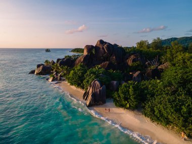 Anse Source dArgent plajı, La Digue Adası, Seyshelles, İHA hava görüntüsü La Digue Seyşelles kuş bakışı, gün batımında sahilde yürüyen birkaç erkek ve kadın lüks bir tatilde
