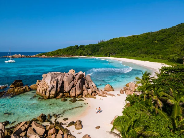 Anse Cocos plajı, La Digue Adası, Seyshelles, La Digue Seychelles kuş bakışı drone görüntüsü, günbatımında kumsalda yürüyen birkaç erkek ve kadın lüks bir tatilde.