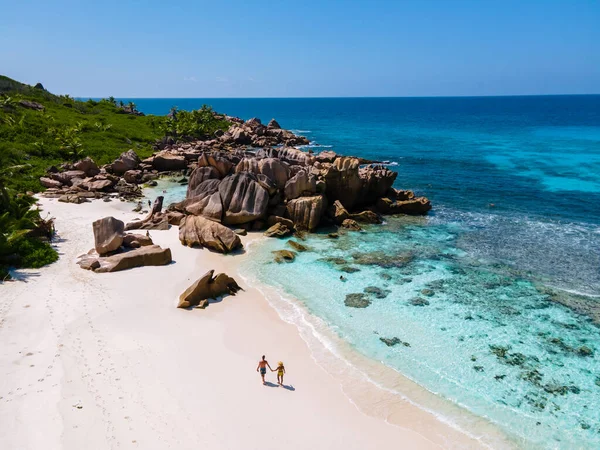 Anse Cocos plajı, La Digue Adası, Seyshelles, La Digue Seychelles kuş bakışı drone görüntüsü, günbatımında kumsalda yürüyen birkaç erkek ve kadın lüks bir tatilde.