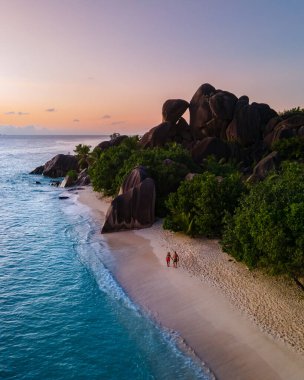 Anse Source dArgent plajı, La Digue Adası, Seyshelles, İHA hava görüntüsü La Digue Seyşelles kuş bakışı, gün batımında sahilde yürüyen birkaç erkek ve kadın lüks bir tatilde