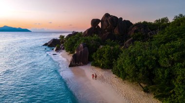 Anse Source dArgent plajı, La Digue Adası, Seyshelles, İHA hava görüntüsü La Digue Seyşelles kuş bakışı, gün batımında sahilde yürüyen birkaç erkek ve kadın lüks bir tatilde