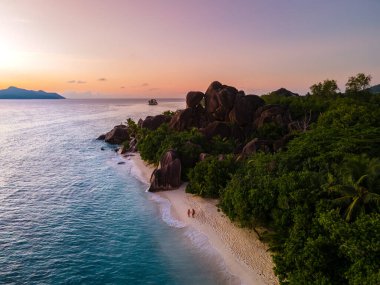 Anse Source dArgent plajı, La Digue Adası, Seyshelles, İHA hava görüntüsü La Digue Seyşelles kuş bakışı, gün batımında sahilde yürüyen birkaç erkek ve kadın lüks bir tatilde