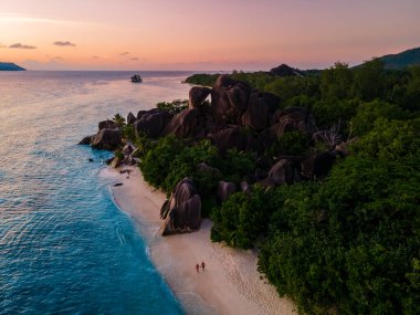 Anse Source dArgent plajı, La Digue Adası, Seyshelles, İHA hava görüntüsü La Digue Seyşelles kuş bakışı, gün batımında sahilde yürüyen birkaç erkek ve kadın lüks bir tatilde
