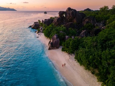 Anse Source dArgent plajı, La Digue Adası, Seyshelles, İHA hava görüntüsü La Digue Seyşelles kuş bakışı, gün batımında sahilde yürüyen birkaç erkek ve kadın lüks bir tatilde