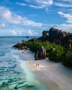 Anse Source dArgent plajı, La Digue Adası, Seyshelles, İHA hava görüntüsü La Digue Seyşelles kuş bakışı, gün batımında sahilde yürüyen birkaç erkek ve kadın lüks bir tatilde