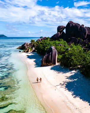 Anse Source dArgent plajı, La Digue Adası, Seyshelles, İHA hava görüntüsü La Digue Seyşelles kuş bakışı, gün batımında sahilde yürüyen birkaç erkek ve kadın lüks bir tatilde