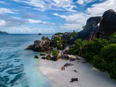 Anse Source dArgent plajı, La Digue Adası, Seyshelles, İHA hava görüntüsü La Digue Seyşelles kuş bakışı, gün batımında sahilde yürüyen birkaç erkek ve kadın lüks bir tatilde