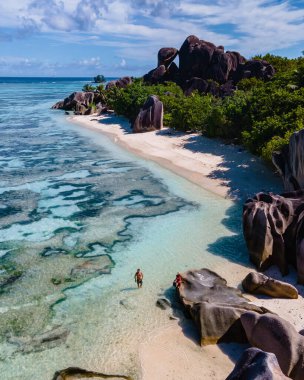Anse Source dArgent plajı, La Digue Adası, Seyshelles, İHA hava görüntüsü La Digue Seyşelles kuş bakışı, gün batımında sahilde yürüyen birkaç erkek ve kadın lüks bir tatilde