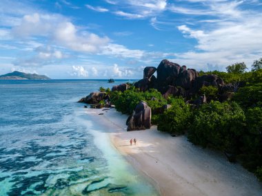Anse Source dArgent plajı, La Digue Adası, Seyshelles, İHA hava görüntüsü La Digue Seyşelles kuş bakışı, gün batımında sahilde yürüyen birkaç erkek ve kadın lüks bir tatilde