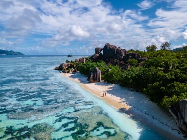 Anse Source dArgent plajı, La Digue Adası, Seyshelles, İHA hava görüntüsü La Digue Seyşelles kuş bakışı, gün batımında sahilde yürüyen birkaç erkek ve kadın lüks bir tatilde