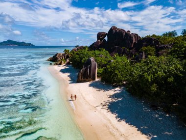Anse Source dArgent plajı, La Digue Adası, Seyshelles, İHA hava görüntüsü La Digue Seyşelles kuş bakışı, gün batımında sahilde yürüyen birkaç erkek ve kadın lüks bir tatilde
