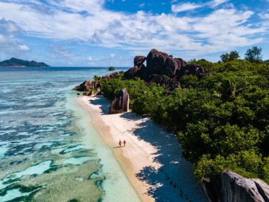 Anse Source dArgent plajı, La Digue Adası, Seyshelles, İHA hava görüntüsü La Digue Seyşelles kuş bakışı, gün batımında sahilde yürüyen birkaç erkek ve kadın lüks bir tatilde