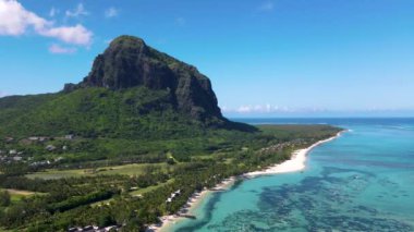 Le Morne plajı Mauritius, Tropikal plaj palmiye ağaçları ve beyaz kum mavisi okyanus ve şemsiyeli plaj yatakları, güneş sandalyeleri ve güneş şemsiyeleri bir palmiye ağacının altında, Le Morne plajı Mauritius 'ta.