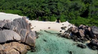 Anse Cocos plajı, La Digue Adası, Seyshelles, La Digue Seychelles kuş bakışı drone görüntüsü, günbatımında kumsalda yürüyen birkaç erkek ve kadın lüks bir tatilde.