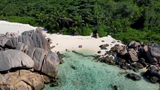 Praia de Anse Cocos, Ilha de La Digue, Seyshelles, Drone vista aérea de La Digue Seychelles vista para os olhos de pássaro, homens de casal e mulher andando na praia durante o pôr do sol em umas férias de luxo — Vídeo de Stock