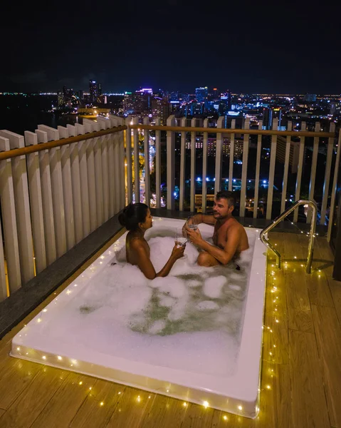 Couple men and woman on a balcony in bathtub looking out over the bay of Pattaya Thailand, men and woman in a jacuzzi. — Stockfoto