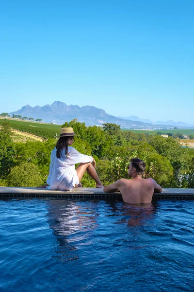 Pareja de hombres y mujeres en la piscina con vistas a los viñedos y montañas de Stellenbosch Sudáfrica —  Fotos de Stock