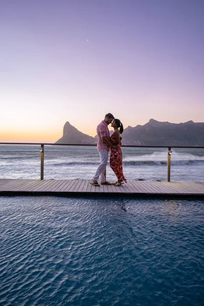 Coppia uomo e donna di fronte alla piscina Infinity affacciata sull'oceano di Città del Capo Sud Africa, uomo e donna in piscina durante il tramonto — Foto Stock