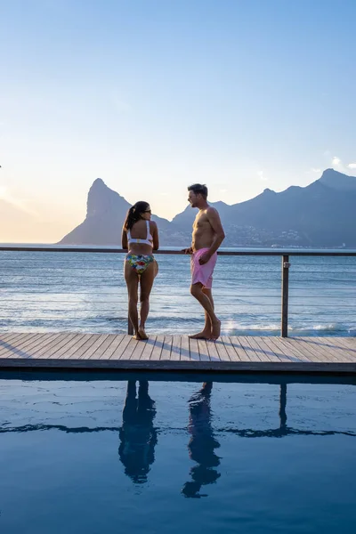 Ζευγάρι άνδρας και γυναίκα μπροστά από Infinity πισίνα με θέα στον ωκεανό του Κέιπ Τάουν της Νότιας Αφρικής, άνδρας και γυναίκα στην πισίνα κατά τη διάρκεια του ηλιοβασιλέματος — Φωτογραφία Αρχείου