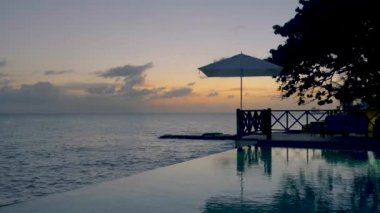 Rahatlatıcı yaz plajı, güneşlenme güvertesi ve sahilde palmiye ağaçları ve Curacao lüks evindeki panoramik deniz manzaralı özel yüzme havuzu.