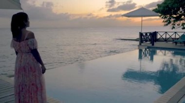 Rahatlatıcı yaz plajı, güneşlenme güvertesi ve sahilde palmiye ağaçları ve Curacao lüks evindeki panoramik deniz manzaralı özel yüzme havuzu.