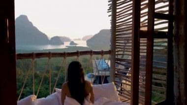 Tayland 'da tatilde olan orta yaşlı bir kadın yatak odasında uyanıp okyanusun üzerinde ve Phnanga Tayland ormanında güneşin doğuşunu seyrediyor.