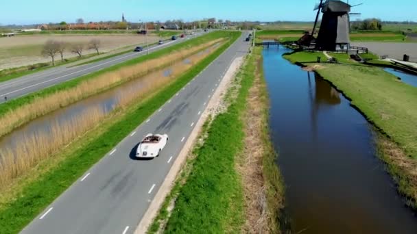 Schermerhorn Alkmaar Netherlands Апрель 2020,. Пара, путешествующая со старым винтажным спортивным автомобилем White Porsche 356 Speedster, голландская ветряная мельница деревня Шермерхорн — стоковое видео