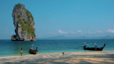 Tayland 'daki Koh Poda tropik plajı, beyaz bir tropik plajda yürüyen turist, arka planda uzun kuyruklu teknesi olan Railay plajı.