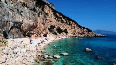 Golfo di Orosei Sardina, yukarıdan manzara, plaj şemsiyeleriyle dolu bir plaj manzarası ve turkuaz suda güneşlenen ve yüzen insanlar. Cala Gonone, Sardinya, İtalya, Cala Mariolu.
