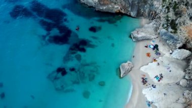 Golfo di Orosei Sardina, yukarıdan manzara, plaj şemsiyeleriyle dolu bir plaj manzarası ve turkuaz suda güneşlenen ve yüzen insanlar. Cala Gonone, Sardinya, İtalya, Cala Mariolu.