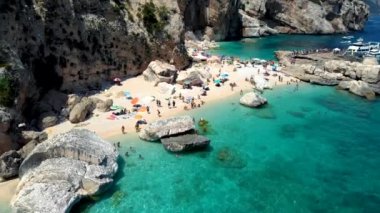 Golfo di Orosei Sardina, yukarıdan manzara, plaj şemsiyeleriyle dolu bir plaj manzarası ve turkuaz suda güneşlenen ve yüzen insanlar. Cala Gonone, Sardinya, İtalya, Cala Mariolu.