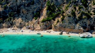 Golfo di Orosei Sardina, yukarıdan manzara, plaj şemsiyeleriyle dolu bir plaj manzarası ve turkuaz suda güneşlenen ve yüzen insanlar. Cala Gonone, Sardinya, İtalya, Cala Mariolu.