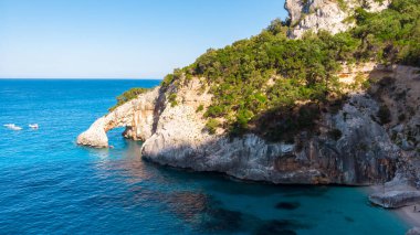 Golfo di Orosei Sardina, yukarıdan manzara, plaj şemsiyeleriyle dolu bir plaj manzarası ve turkuaz suda güneşlenen ve yüzen insanlar. Cala Gonone, Sardinya, İtalya, Cala Mariolu.