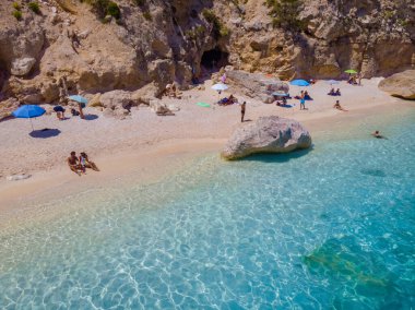 Golfo di Orosei Sardina, yukarıdan manzara, plaj şemsiyeleriyle dolu bir plaj manzarası ve turkuaz suda güneşlenen ve yüzen insanlar. Cala Gonone, Sardinya, İtalya, Cala Mariolu.