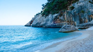 Golfo di Orosei Sardina, yukarıdan manzara, plaj şemsiyeleriyle dolu bir plaj manzarası ve turkuaz suda güneşlenen ve yüzen insanlar. Cala Gonone, Sardinya, İtalya, Cala Mariolu.